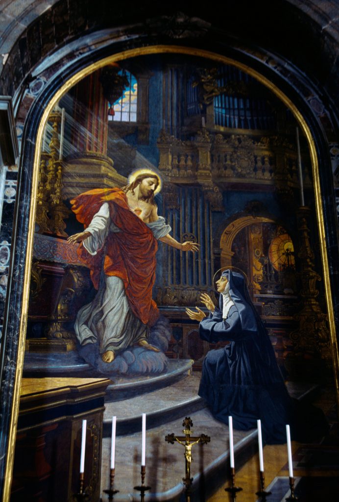 Photograph of a mosaic depicting Jesus in a white robe with a red sash draped over him and his Sacred Heart shown to a nun kneeling before Him in a black habit.